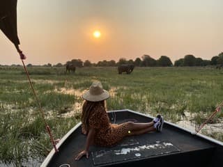 A solo woman traveler resting on a boat at sunset in Botswana